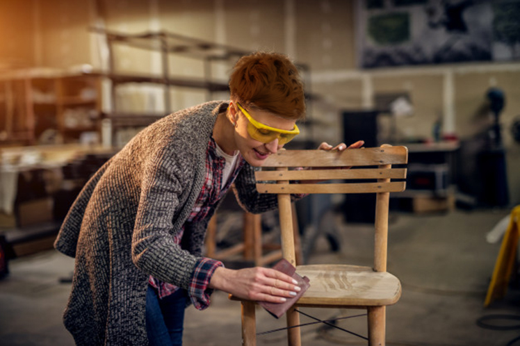Mujer lijando un silla Oficio carpinteria